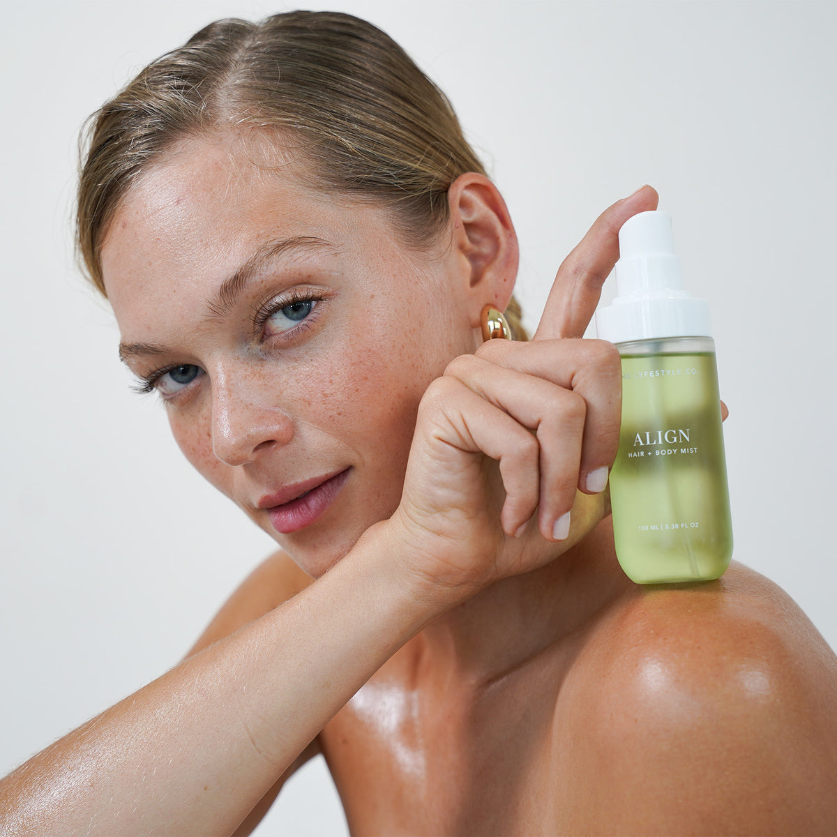Model holding The Lyfestyle Co. Align Hair & Body Mist against her shoulder.