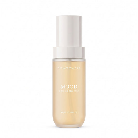 A bottle of The Lyfestyle Co. Mood Hair & Body Mist, featuring a frosted plastic bottle filled with a light orange liquid and a white spray dispenser, set against a plain white background.